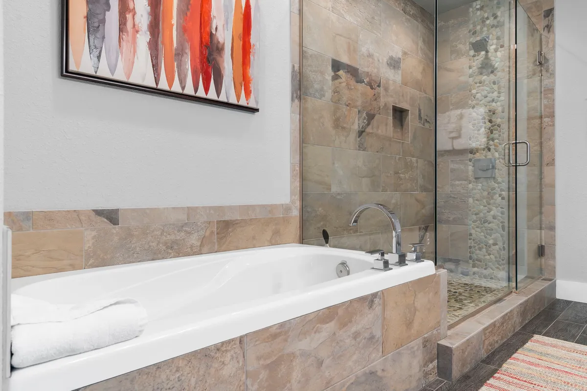 A tranquil bathroom scene highlighting a spacious bathtub and modern shower area, accented by tasteful wall art. The atmosphere is calming, suggesting a comfortable and private ensuite space within the loft.