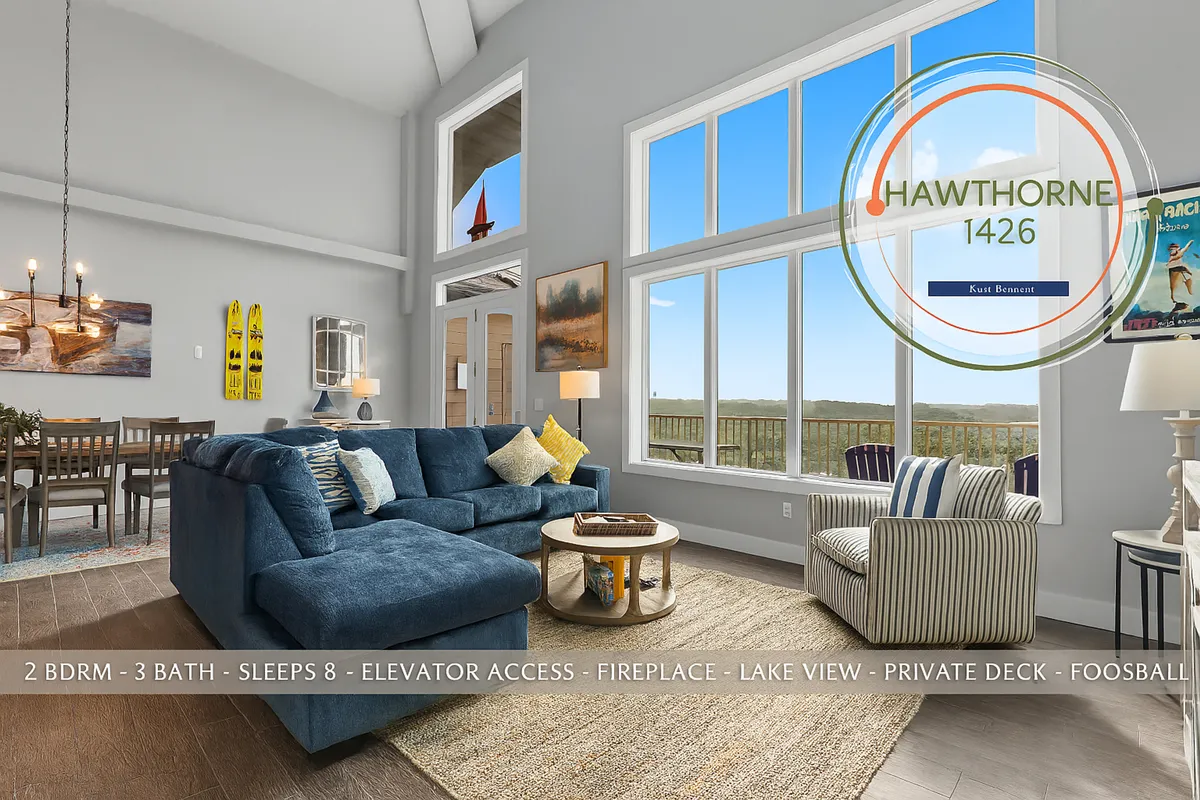 A spacious open-concept living area featuring a large sectional sofa, a stylish dining area with a chandelier, expansive windows offering stunning lake views, decorative artwork, and a foosball table in the corner. Natural light pours into the space, highlighting the cozy and inviting ambiance that encourages both relaxation and social gatherings.