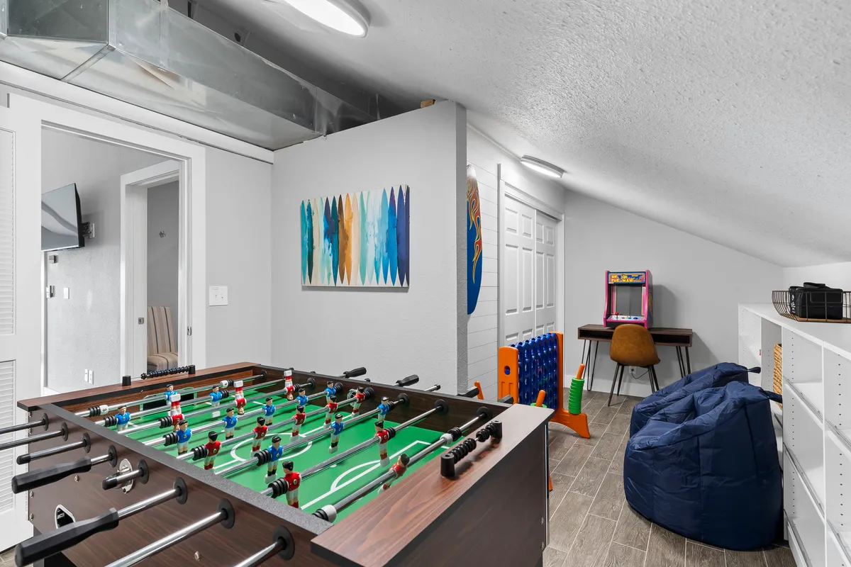 A lively game area featuring a foosball table as the centerpiece, vibrant wall art, a classic arcade game, and a cozy bean bag chair. The space radiates playful energy and is designed for interactive fun, with elements that invite friendly competition and relaxation.