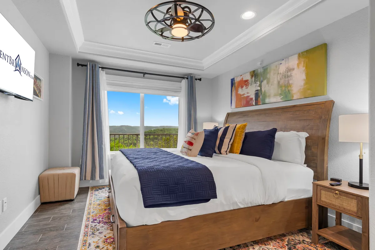 A cozy king bedroom featuring a plush bed, large window with scenic views, artistic wall decor, and a soft lighting fixture. The window frames tranquil outdoor scenery, making the room feel restful and inviting.