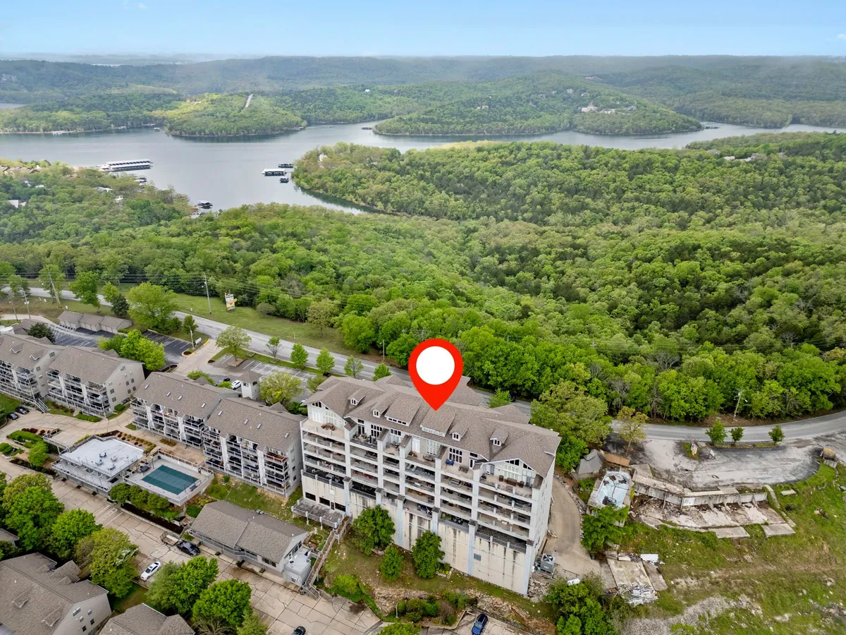 This exterior image captures the waterfront view with lush greenery, residential buildings, and a sparkling swimming pool, all under a serene sky. The pool area is central, suggesting a fun and inviting community atmosphere perfect for summer activities.