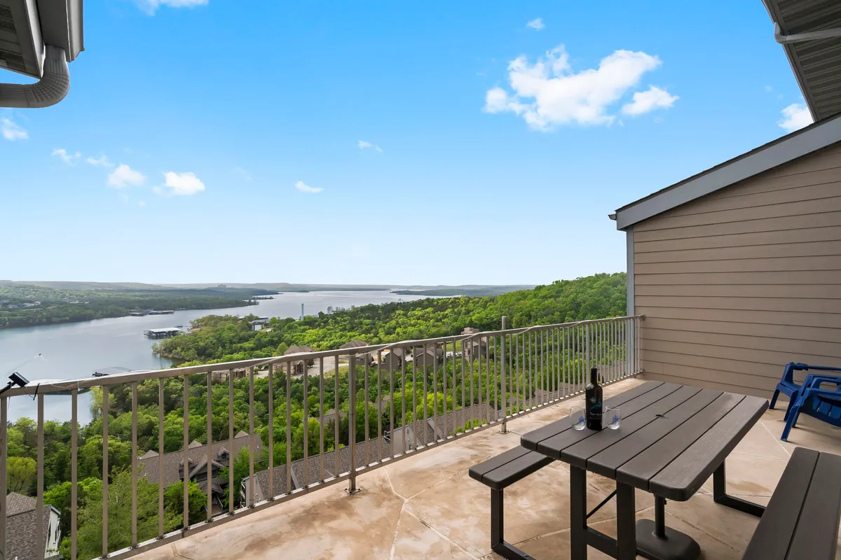 This image captures a serene outdoor deck with a table and chairs set up facing a breathtaking view of Table Rock Lake. A bottle of wine sits on the table, inviting guests to relax and savor drinks or meals while soaking in the scenery. The deck’s rail ensures safety and a sense of privacy, making it a perfect spot for both quiet reflection and social gatherings.