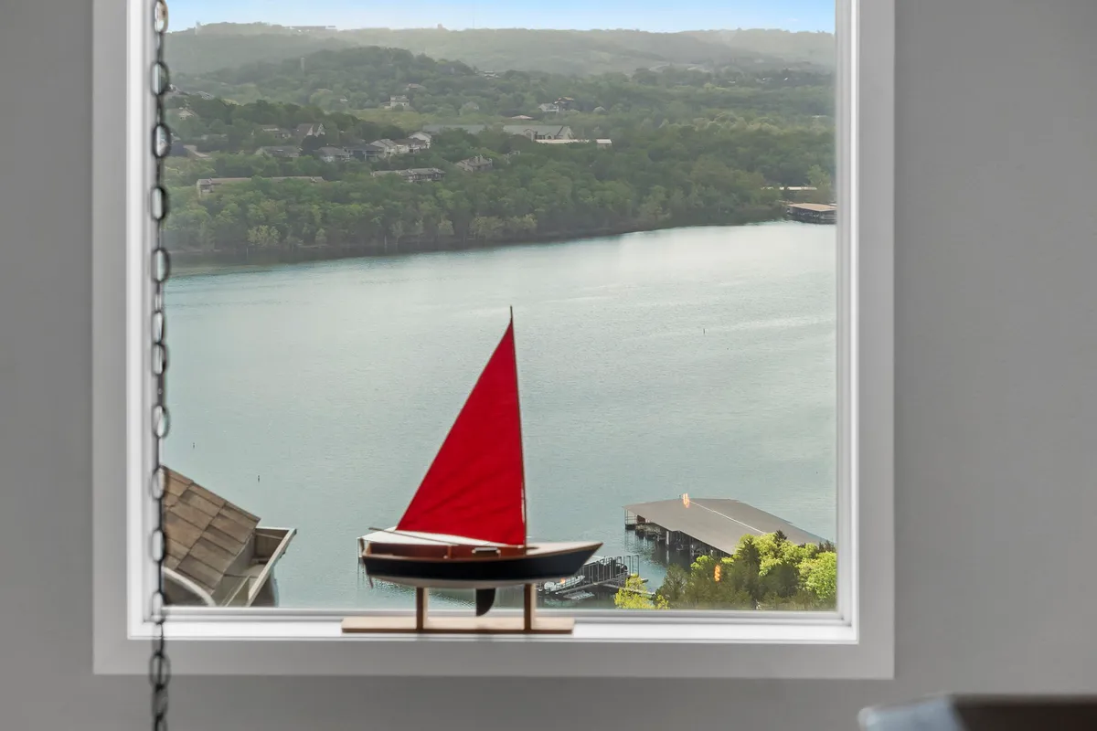 A captivating water view featuring a red sailboat gliding on the lake, with lush green hills in the background. The scene exudes relaxation and adventure, highlighting the recreational and scenic opportunities just steps from the retreat.