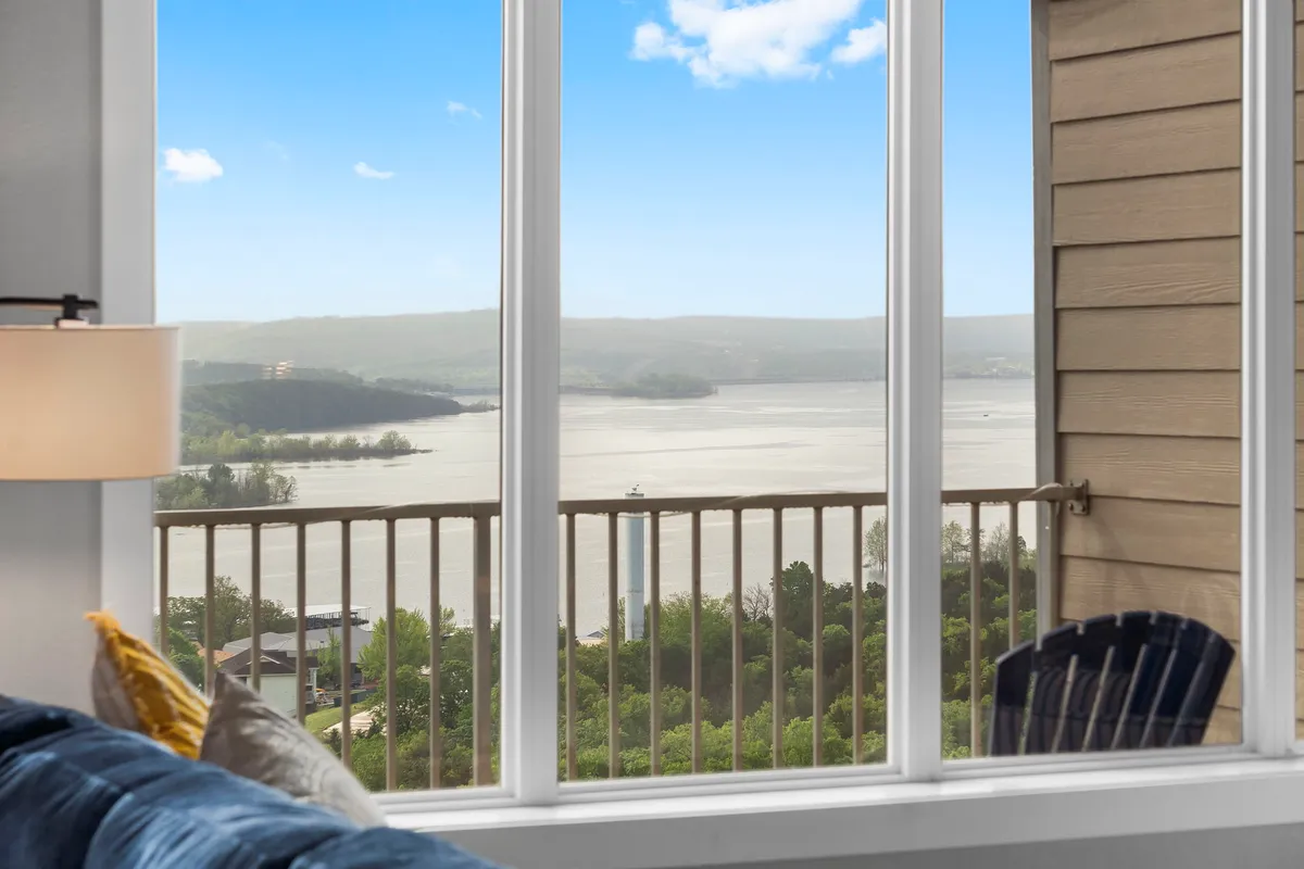 A view from inside looking out through expansive windows onto a serene water surface and distant hills. The composition emphasizes the tranquil connection between indoor relaxation and the natural beauty outside, capturing the peacefulness and allure of lakeside living.