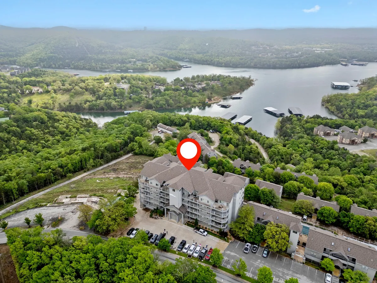 A panoramic lake view framed by rolling hills and an apartment complex, capturing the expansive beauty of Table Rock Lake and the surrounding natural landscape. The water is calm, inviting activities like boating, fishing, and picnicking.