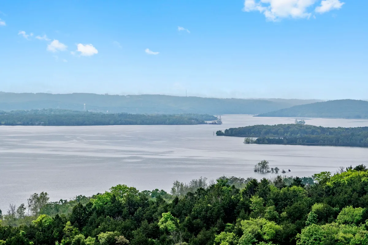 The image showcases a breathtaking, wide-angle view of the expansive lake framed by rolling distant hills and lush greenery. A golden sunset casts a warm glow over the water, evoking tranquility and inviting guests to relax in nature's beauty. The peaceful setting hints at outdoor activities like boating, fishing, and lakeside picnics, while the open skies promise unforgettable stargazing and wildlife sightings.