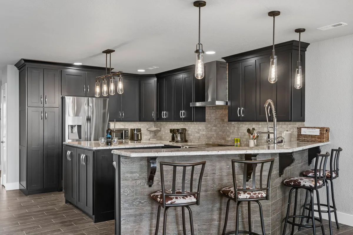 A modern kitchen highlighted by a large island with seating, rich cabinetry, and stylish lighting fixtures. The kitchen is open to the living space, making it ideal for both culinary creativity and socializing, with a warm, welcoming mood.